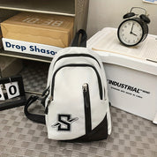 Zaino bianco e nero con logo "S", tasche multiple, su pavimento a scacchi. Orologio vintage e scatola industriale sullo sfondo.