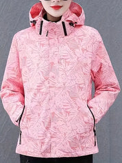 Giacca impermeabile donna rosa con cappuccio, motivo foglie tropicali, chiusura zip, tasche laterali. Abbigliamento outdoor moda autunno inverno.