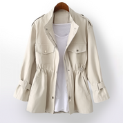 Giacca beige da donna con tasche frontali, cintura regolabile e bottoni, su sfondo bianco. Moda femminile, abbigliamento casual elegante.