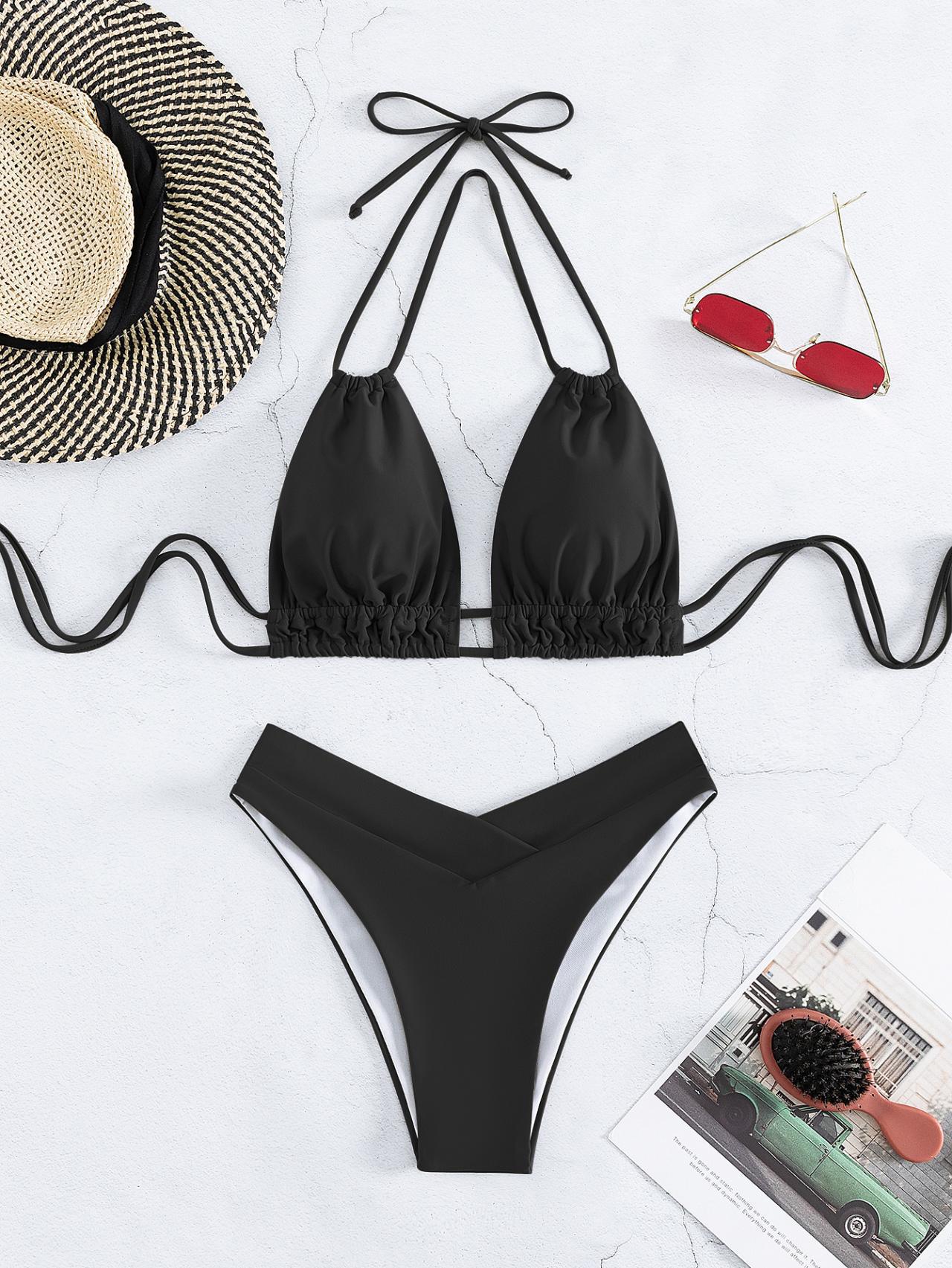 Bikini nero a triangolo con laccetti, slip a vita bassa. Accessori: cappello di paglia, occhiali da sole rossi, rivista. Moda mare estate.