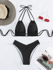 Bikini nero a triangolo con laccetti, slip a vita bassa. Accessori: cappello di paglia, occhiali da sole rossi, rivista. Moda mare estate.