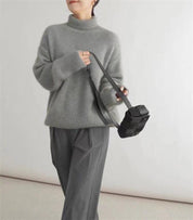 Donna con maglione grigio a collo alto, pantaloni grigi e borsa a tracolla nera. Moda autunnale, abbigliamento casual elegante.