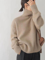 Donna con maglione beige a collo alto, borsa a tracolla marrone, orecchini dorati. Moda autunnale, abbigliamento casual elegante.