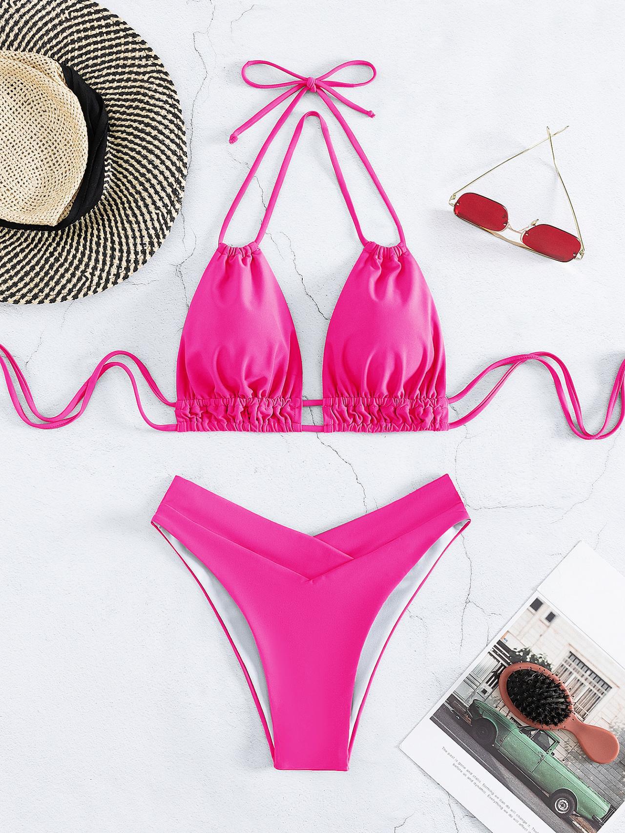 Bikini rosa a triangolo con laccetti, occhiali da sole rossi, cappello di paglia e rivista su sfondo bianco. Moda mare estiva donna.
