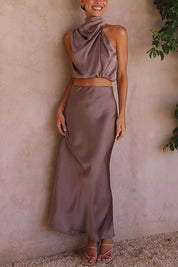 Abito lungo elegante in raso color taupe, senza maniche, con collo alto e spacco laterale. Perfetto per eventi serali e cerimonie.