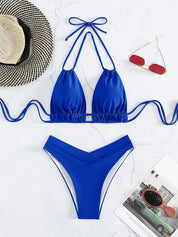 Bikini blu a due pezzi con laccetti, cappello di paglia, occhiali da sole rossi e rivista su sfondo bianco. Moda mare estiva donna.