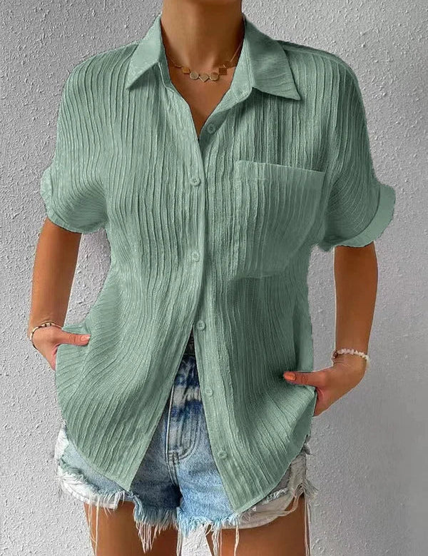 Camicia verde a maniche corte in tessuto plissettato, con colletto classico e taschino, abbinata a shorts di jeans. Moda estiva casual donna.