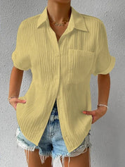 Camicia gialla a maniche corte in tessuto plissettato, abbinata a shorts di jeans. Look estivo casual per donna.
