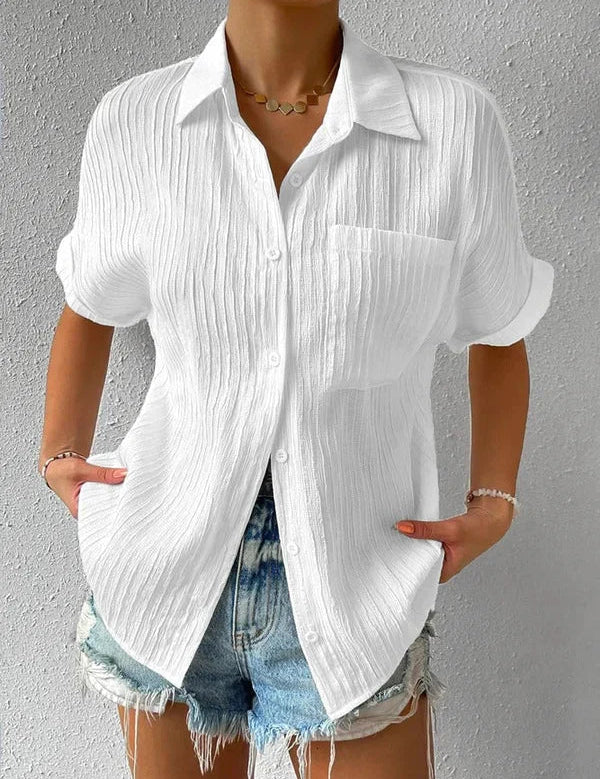 Camicia bianca a maniche corte in tessuto leggero, con colletto classico e taschino, abbinata a shorts di jeans. Look estivo casual donna.