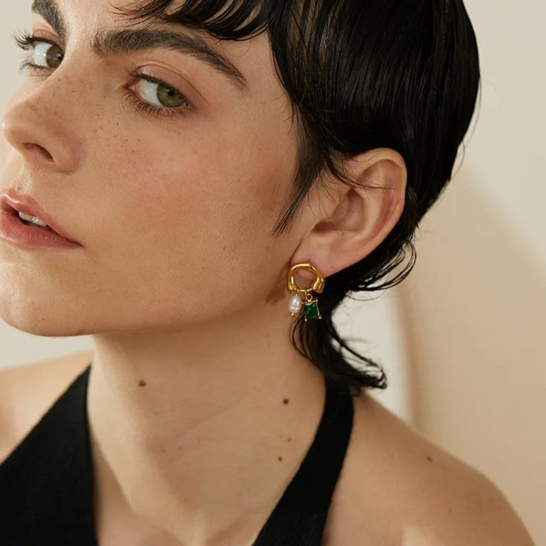 Orecchino pendente oro con perla e pietra verde su donna con capelli corti neri. Gioielli eleganti, moda femminile, accessori di lusso.