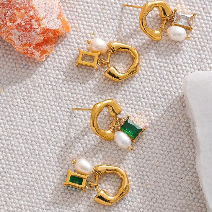 Orecchini pendenti in oro con perle e pietre verdi e trasparenti su sfondo tessuto. Gioielli eleganti, moda donna, accessori di lusso.