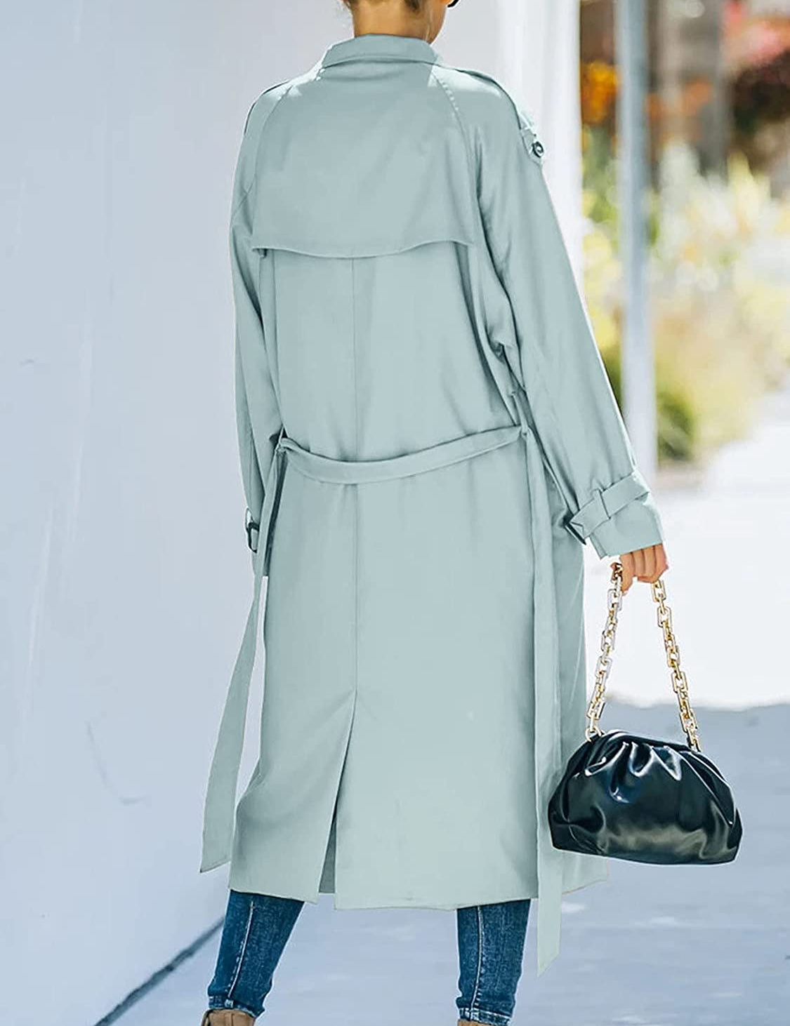 Donna con trench verde chiaro, jeans e borsa nera a catena dorata. Moda autunnale, stile urbano elegante. Sfondo urbano sfocato.