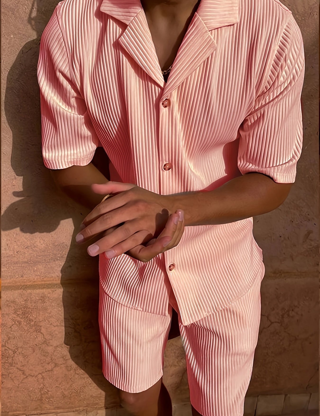 Abbigliamento estivo uomo: completo rosa a righe, camicia a maniche corte e pantaloncini coordinati. Moda casual, tessuto leggero, stile moderno.