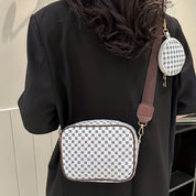 Donna con borsa a tracolla bianca e marrone con motivo a scacchi, abbinata a un piccolo portamonete rotondo. Accessorio moda elegante e moderno.