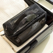 Borsa da viaggio nera in rete trasparente con manico, contenente articoli da toeletta, posizionata all'interno di una valigia aperta su un letto.