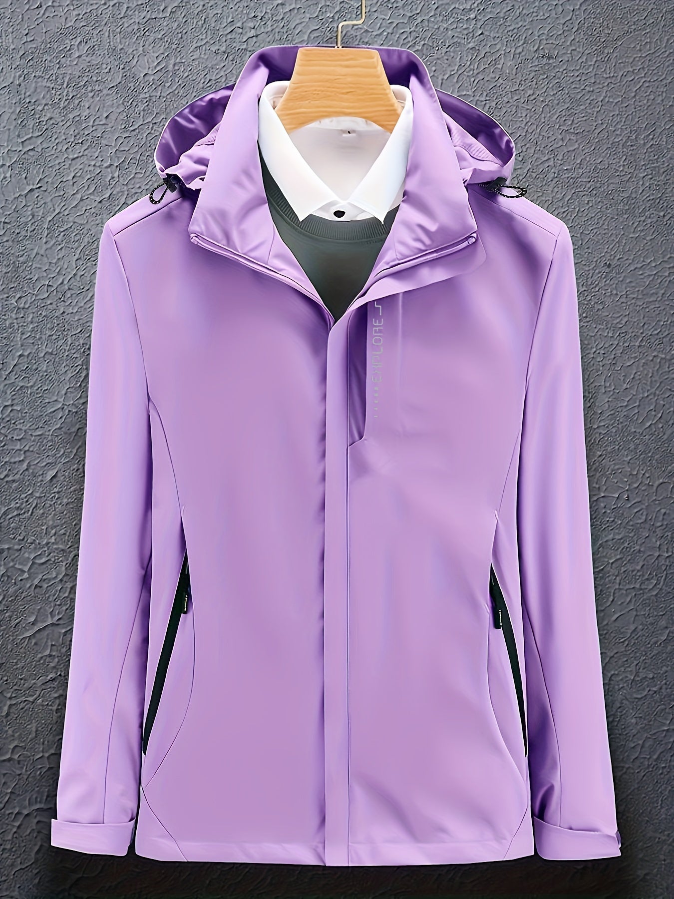 Giacca impermeabile viola con cappuccio, appesa su gruccia, su sfondo grigio. Design elegante, ideale per outdoor e moda autunnale.