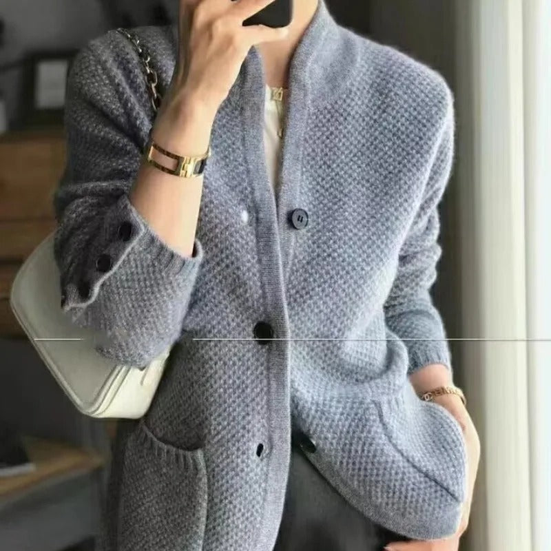 Giacca cardigan donna grigia, tessuto lavorato a maglia, bottoni neri, tasche frontali, abbinata a borsa bianca. Elegante e casual.