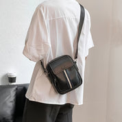 Borsa a tracolla nera in pelle con cerniera, indossata su camicia bianca. Design elegante e moderno, ideale per moda urbana e casual.