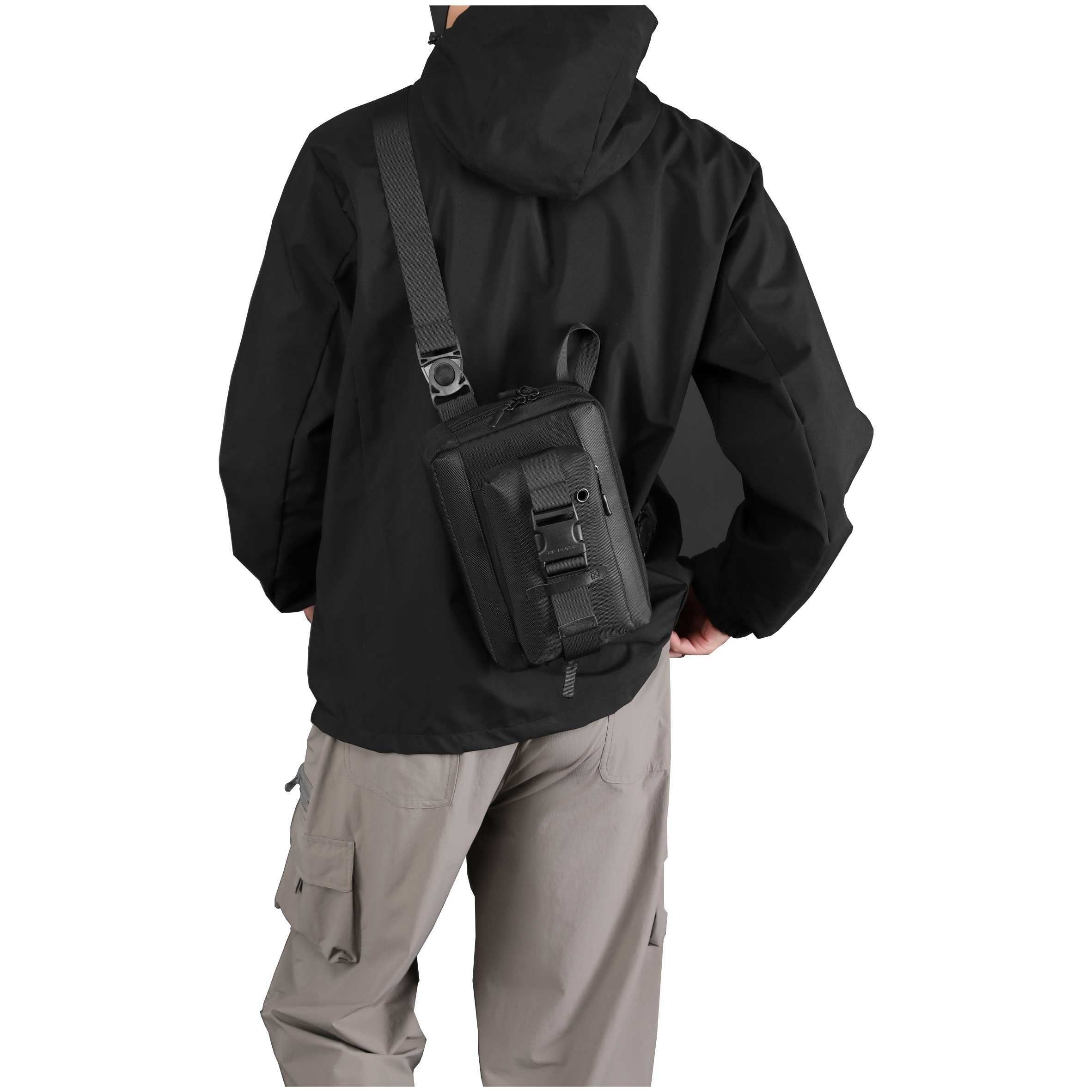 Uomo con giacca nera e pantaloni cargo grigi indossa zaino a tracolla nero. Accessorio moda outdoor, pratico e resistente.