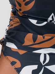 Costume da bagno intero donna con stampa foglie tropicali marroni e bianche su sfondo nero, design arricciato, moda mare estate.