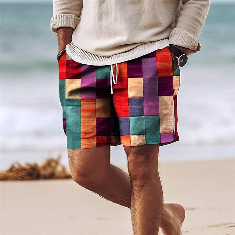 Uomo in spiaggia con pantaloncini patchwork colorati, maglione beige e orologio nero. Moda estiva, abbigliamento casual maschile.