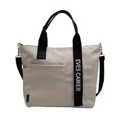 Borsa a tracolla beige con manici neri, tasca frontale e scritta "EVES CAMIER". Design moderno, ideale per moda donna e accessori eleganti.