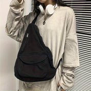 Zaino a tracolla nero unisex, stile casual, con tasca frontale con zip. Indossato con cuffie bianche e maglia oversize beige.