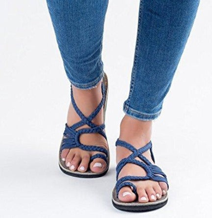 Sandali intrecciati blu su piedi femminili, abbinati a jeans aderenti. Calzature estive eleganti, comode e alla moda per donna.