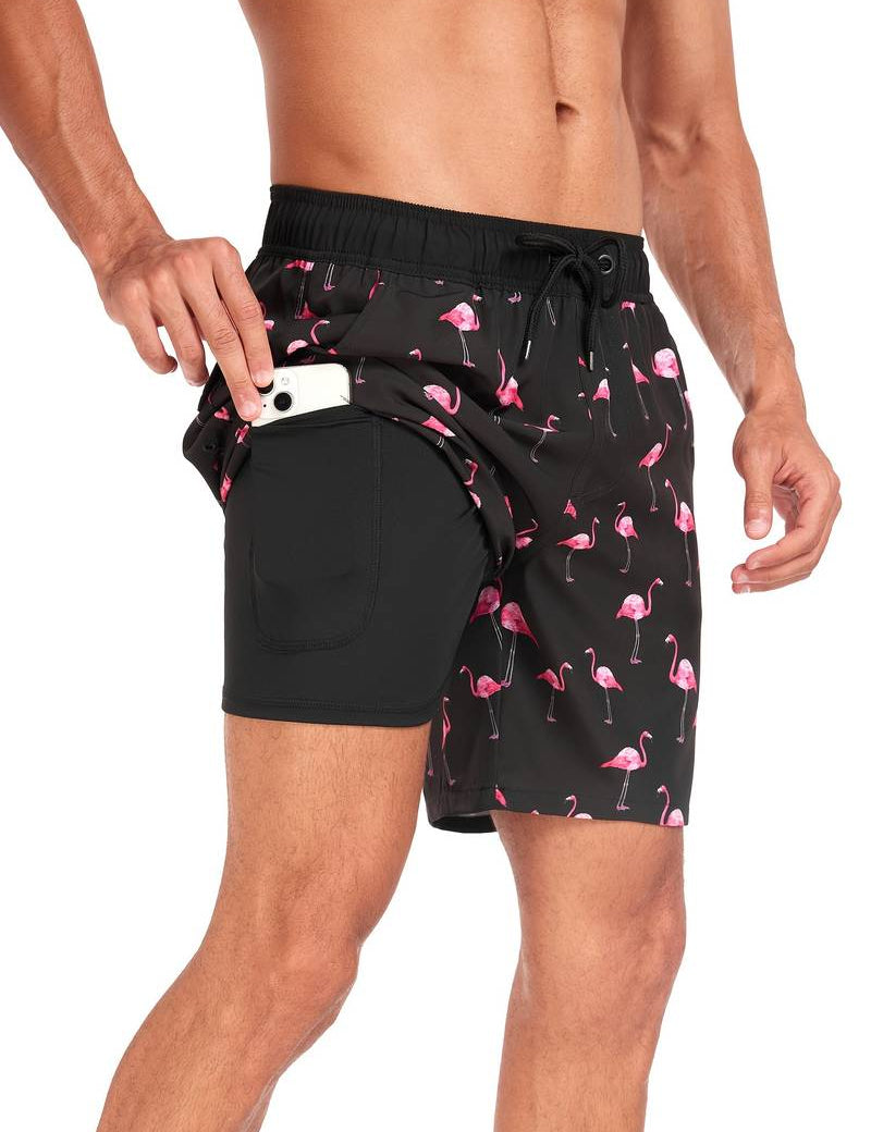 Uomo in costume da bagno nero con fenicotteri rosa, tasca laterale con smartphone. Moda mare, abbigliamento estivo, pantaloncini da nuoto.