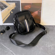 Borsa a tracolla nera in pelle con striscia centrale, design moderno, su sfondo grigio. Accessorio moda uomo, elegante e funzionale.