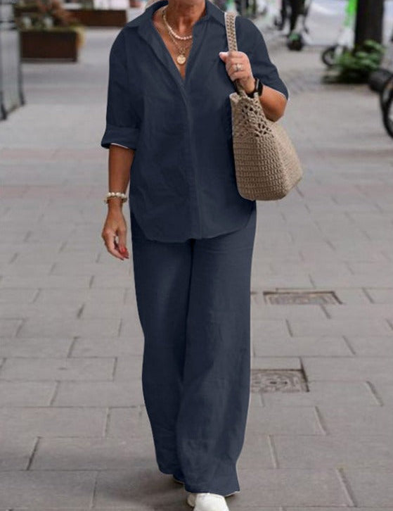 Donna con camicia blu scuro e pantaloni abbinati, borsa a tracolla beige, cammina su marciapiede cittadino. Moda casual elegante, abbigliamento donna.