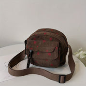 Borsa a tracolla marrone in velluto a coste con motivo a pois rossi, tasca frontale e chiusura a zip. Accessorio moda casual e versatile.