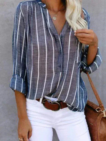 Camicia a righe verticali blu e bianche, maniche lunghe, abbinata a pantaloni bianchi e cintura marrone. Stile casual elegante per donna.