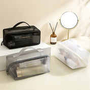 Tre borse da toilette trasparenti su un tavolo, contenenti prodotti per la cura personale. Design elegante, ideale per viaggi e organizzazione.
