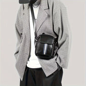 Giacca a quadri grigia da uomo con borsa a tracolla nera in pelle, dettagli a righe, abbinata a t-shirt bianca e pantaloni neri. Moda casual elegante.