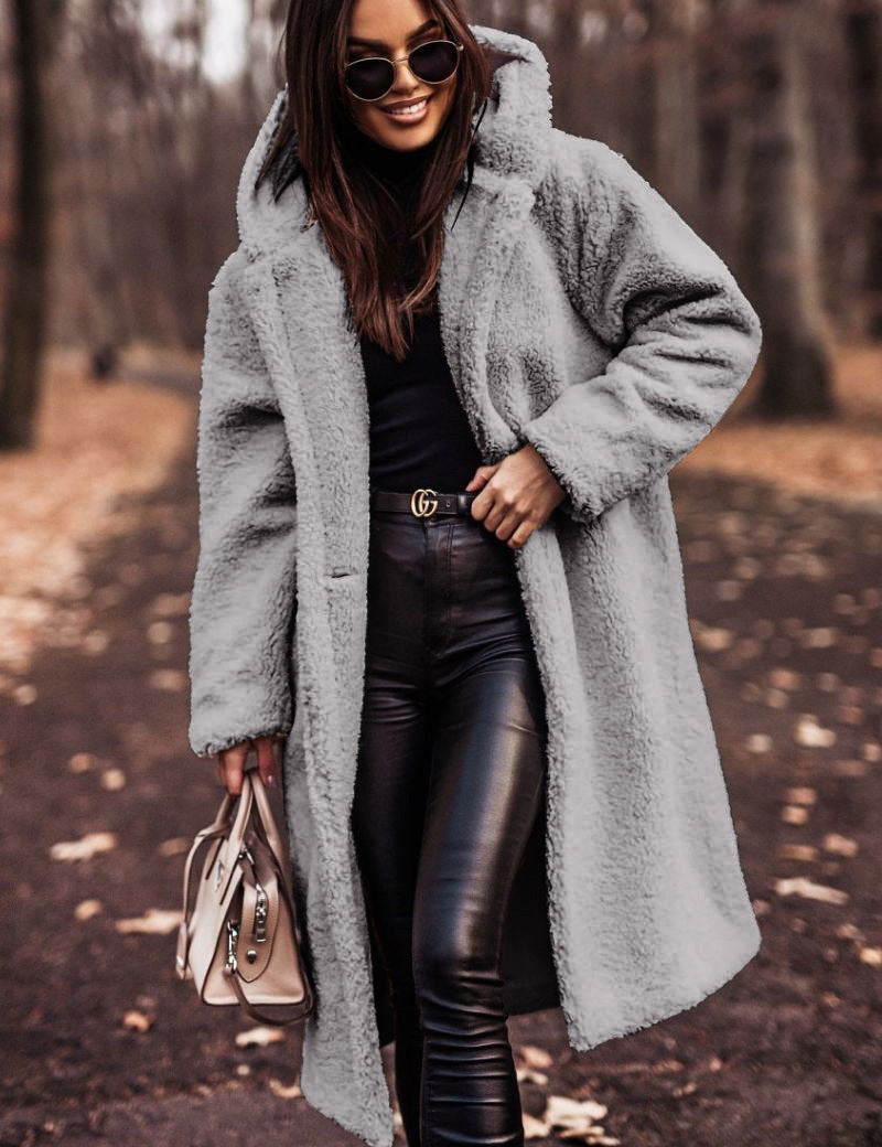 Donna con cappotto in pelliccia sintetica grigia, occhiali da sole, pantaloni in pelle nera, borsa beige, in un parco autunnale. Moda autunno inverno.