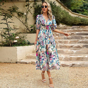 Donna con abito floreale lungo, occhiali da sole e sandali bianchi su gradini di pietra. Moda estiva, abbigliamento femminile elegante.