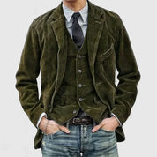 Giacca uomo in velluto a coste verde, abbinata a gilet e cravatta nera, camicia a righe e jeans. Look elegante e casual per moda maschile.
