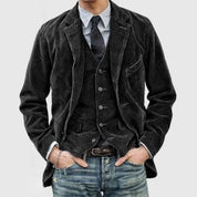 Giacca uomo in velluto nero, abbinata a gilet e cravatta, su camicia a righe. Look casual con jeans. Moda maschile elegante e moderna.