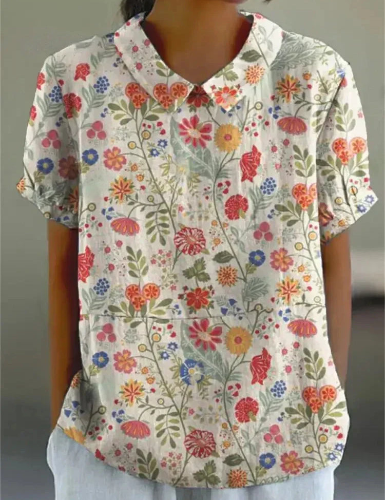 Camicia donna a maniche corte con stampa floreale colorata, colletto classico, sfondo bianco. Moda estiva casual, tessuto leggero e traspirante.