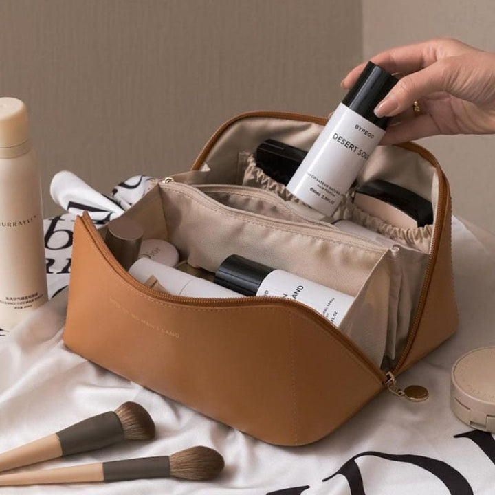 Beauty case in pelle marrone con prodotti cosmetici, tra cui flaconi e pennelli per trucco, su sfondo chiaro. Accessori eleganti per skincare.