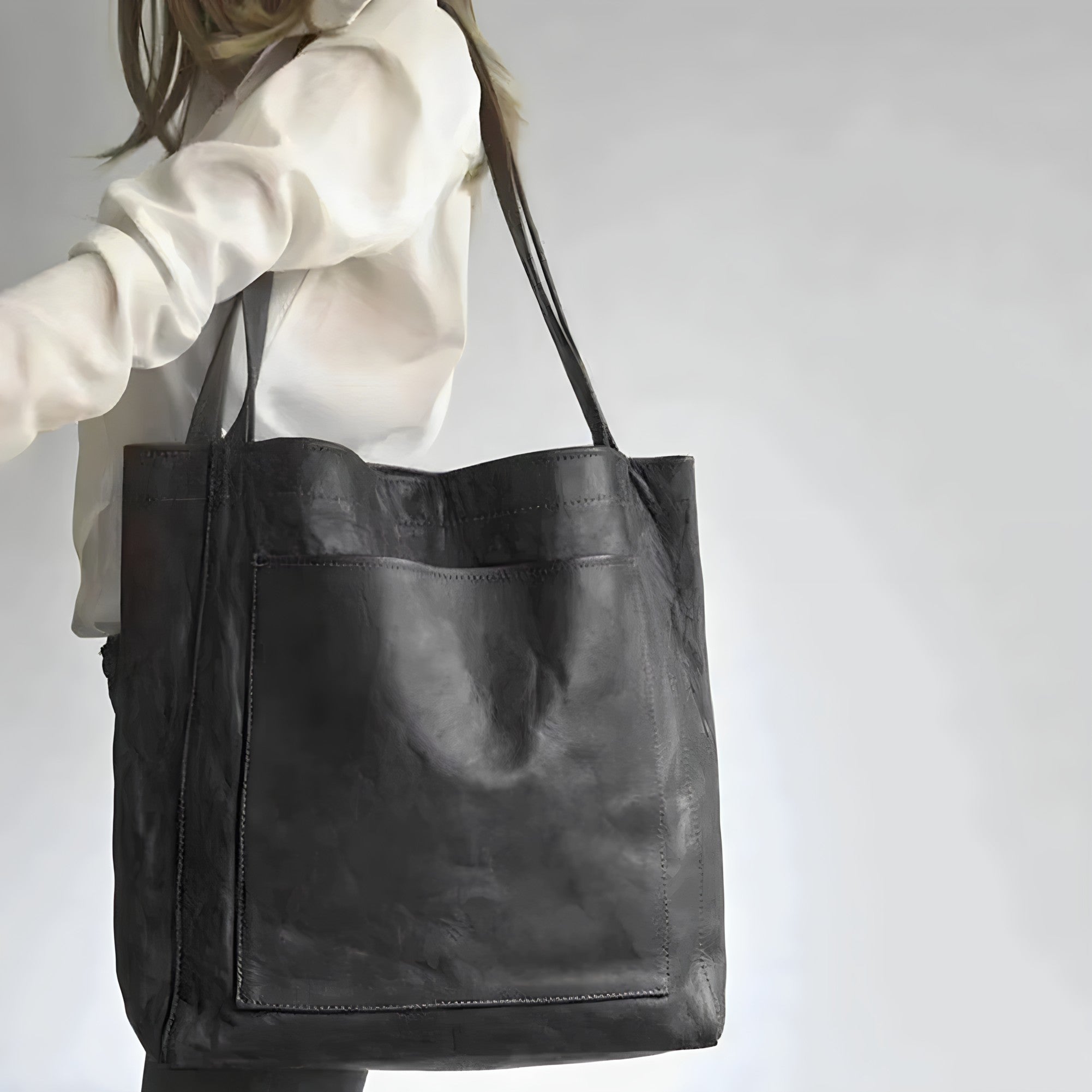 Borsa shopper in pelle nera, elegante e spaziosa, indossata da una donna con camicia bianca. Accessorio moda femminile, ideale per ogni occasione.