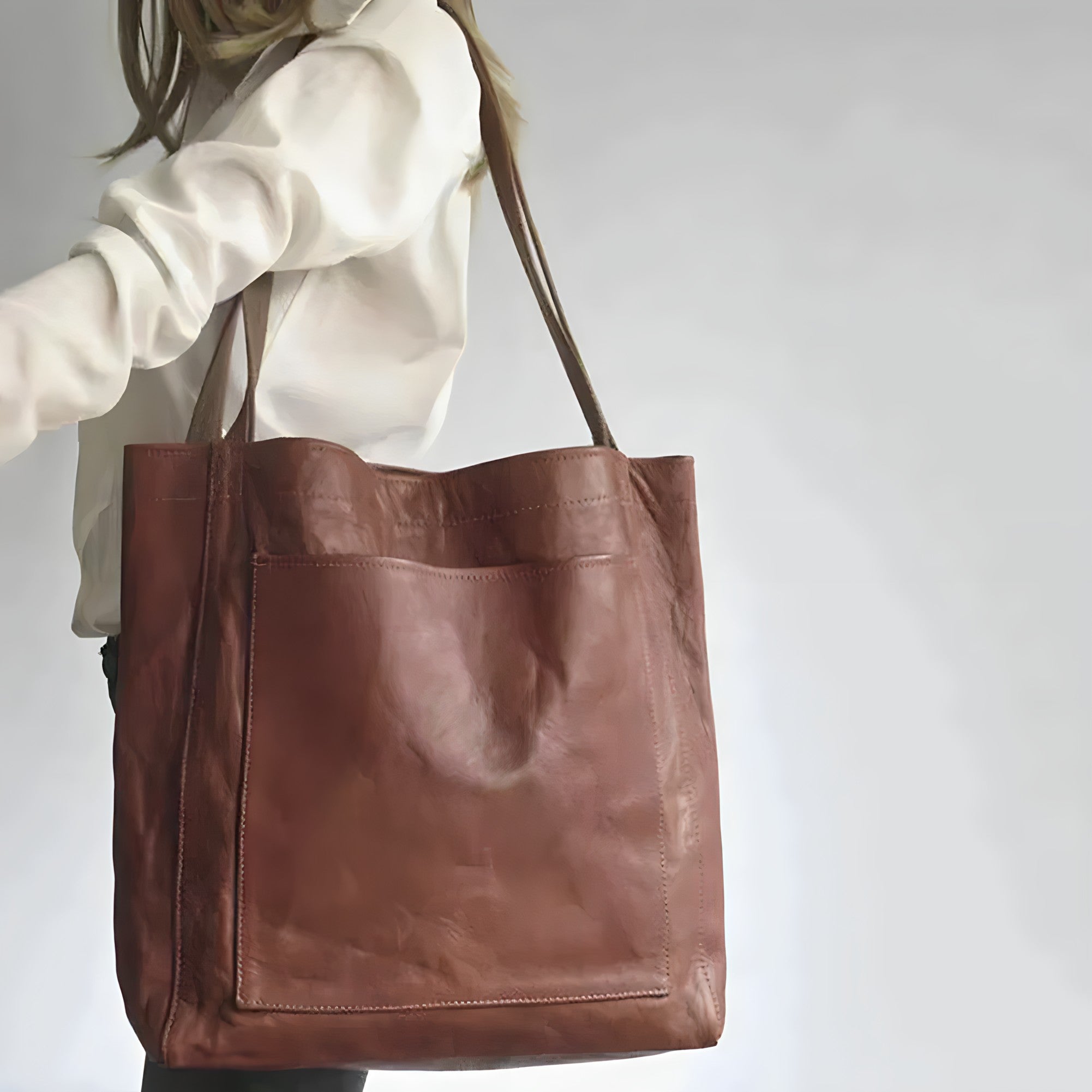 Borsa shopper in pelle marrone, design minimalista, indossata da una donna. Accessorio moda elegante e versatile per ogni occasione.
