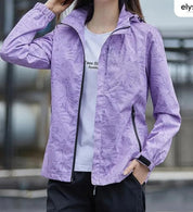 Giacca a vento viola con motivo floreale, zip frontale, tasche laterali, indossata da una donna. Ideale per attività all'aperto e sport.