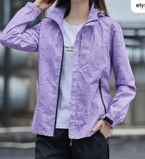 Giacca a vento viola con motivo floreale, zip frontale, tasche laterali, indossata da una donna. Ideale per attività all'aperto e sport.