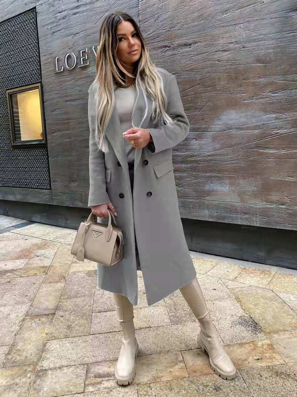 Donna con cappotto grigio elegante, borsa beige e stivali abbinati, posa davanti a un muro moderno. Moda autunnale, stile urbano chic.