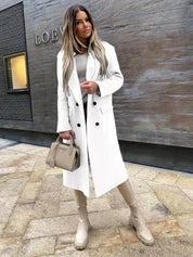 Donna con cappotto bianco elegante, stivali beige e borsa alla moda, posa davanti a un edificio moderno. Look autunnale chic e sofisticato.
