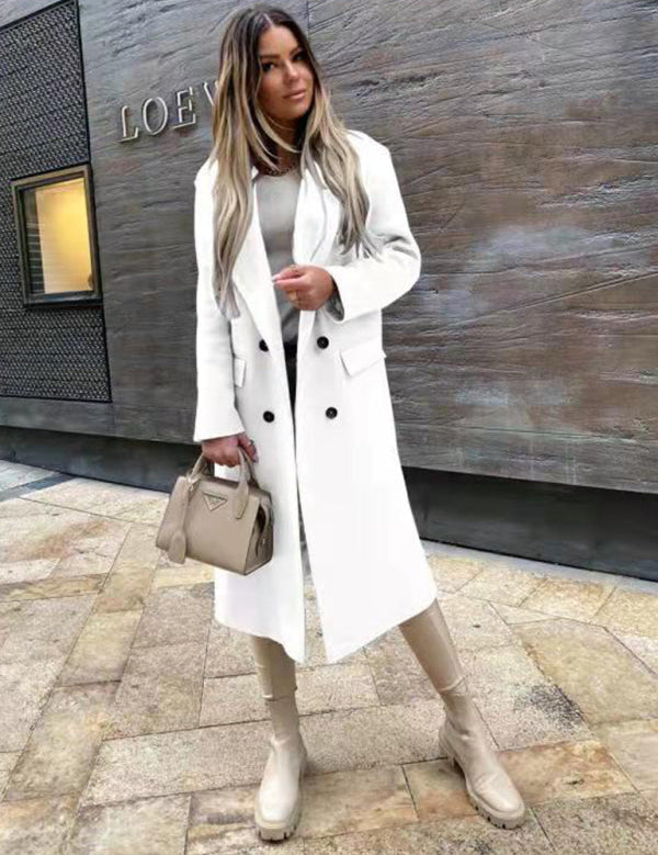 Donna con cappotto bianco elegante, stivali beige e borsa alla moda, posa davanti a un edificio moderno. Look autunnale chic e sofisticato.