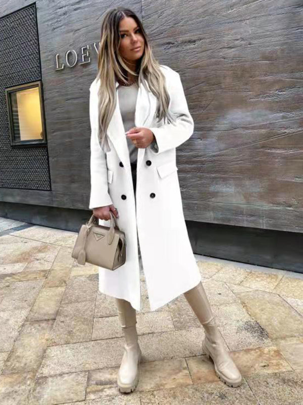 Donna con cappotto bianco elegante, stivali beige e borsa alla moda, posa davanti a un edificio moderno. Look autunnale chic e sofisticato.