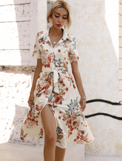 Donna con abito floreale estivo bianco, maniche corte, cintura in vita, sfondo urbano. Moda femminile elegante, abbigliamento casual chic.